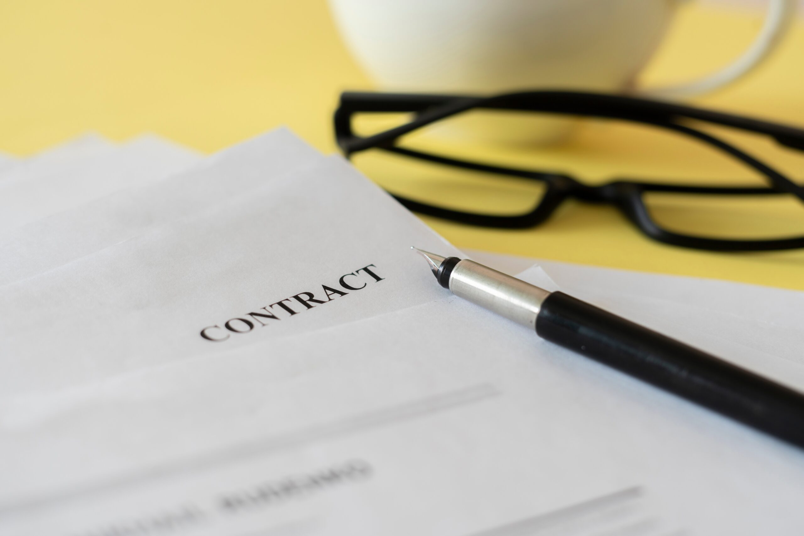 a close up macro view of a contract document with eye glasses and a pen