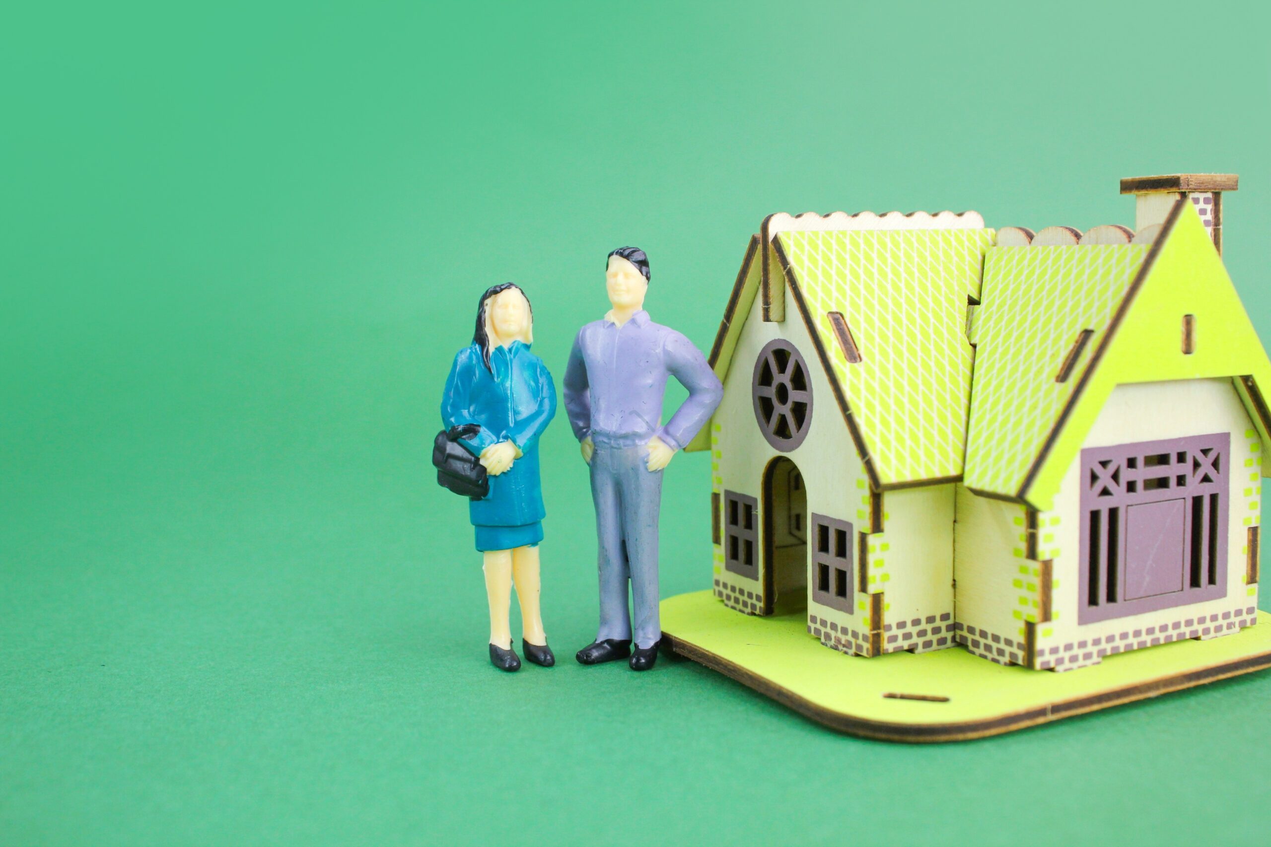 a pair of miniature people with a model house.