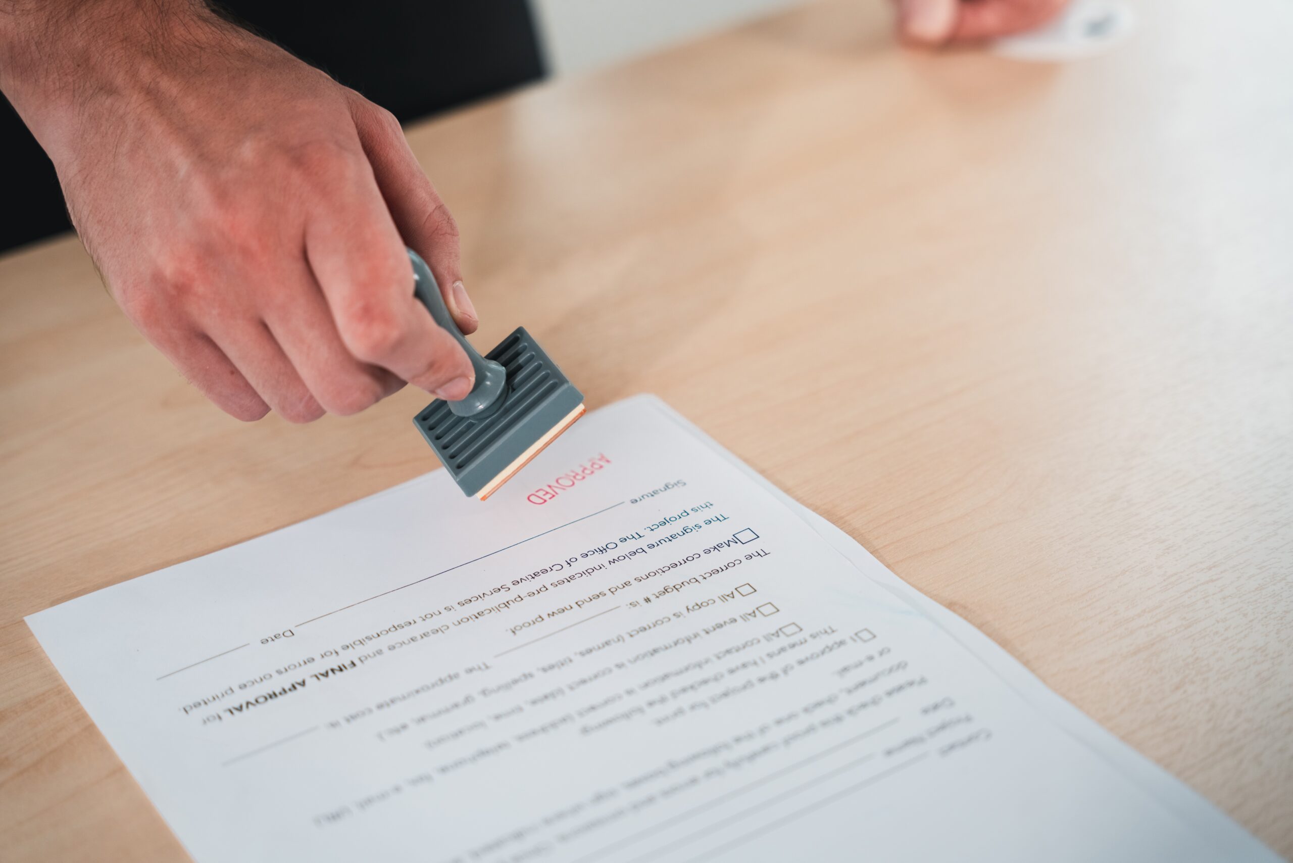 Businessman hand stamping an approved stamp on a text document.