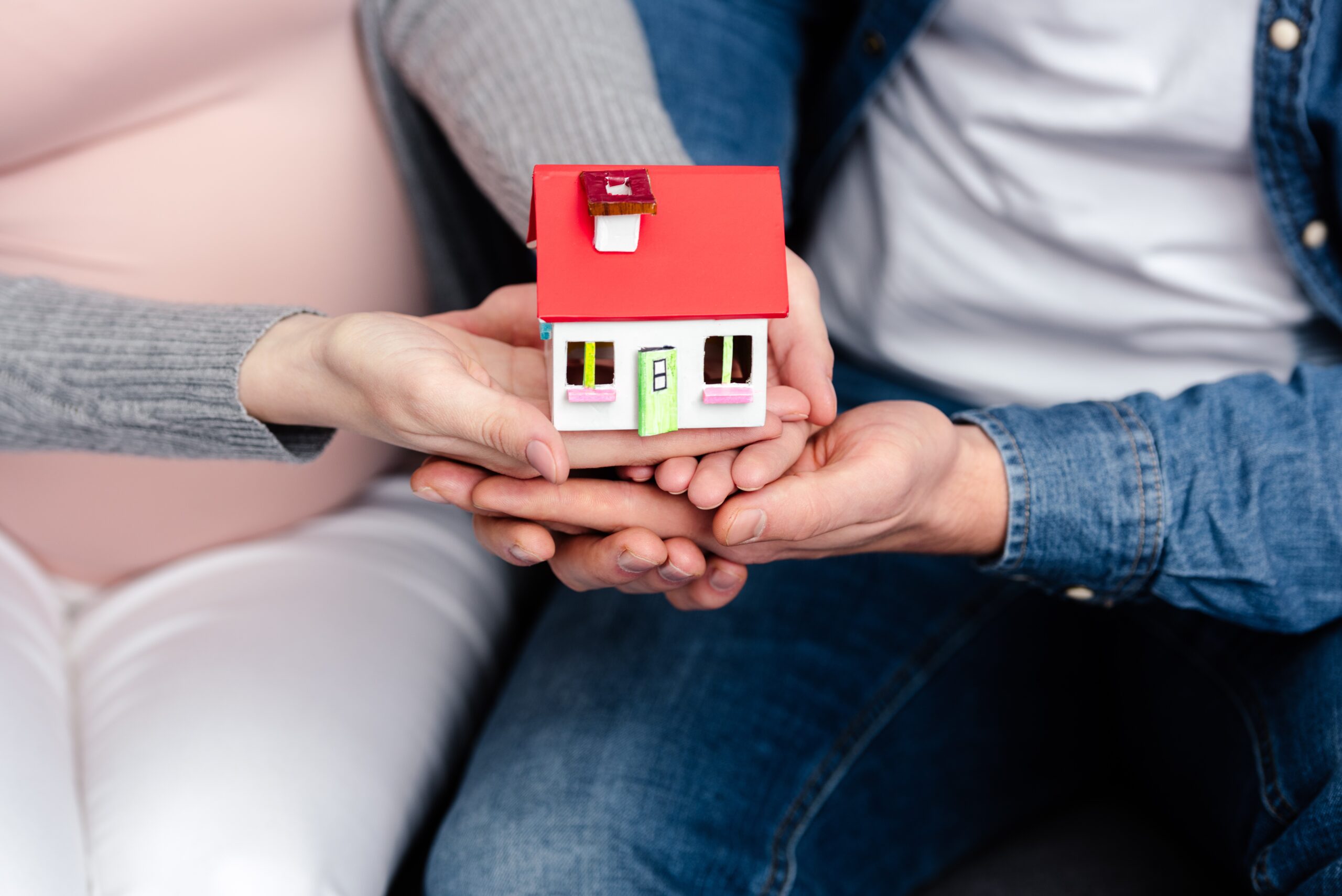 close-up partial view of young pregnant couple holding small house model
