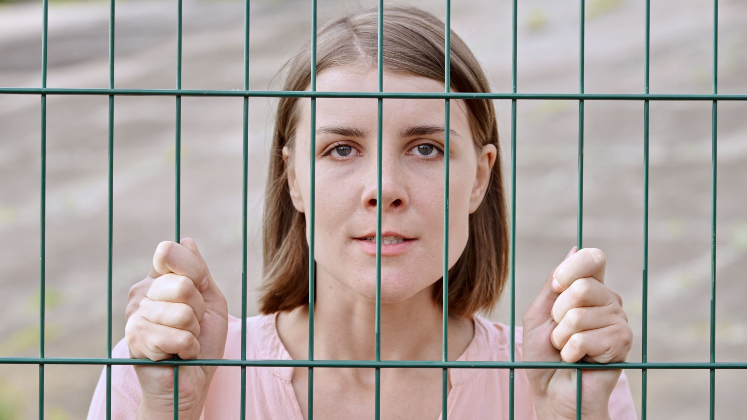 Closeup shot of a caucasian female looking angrily through a gate