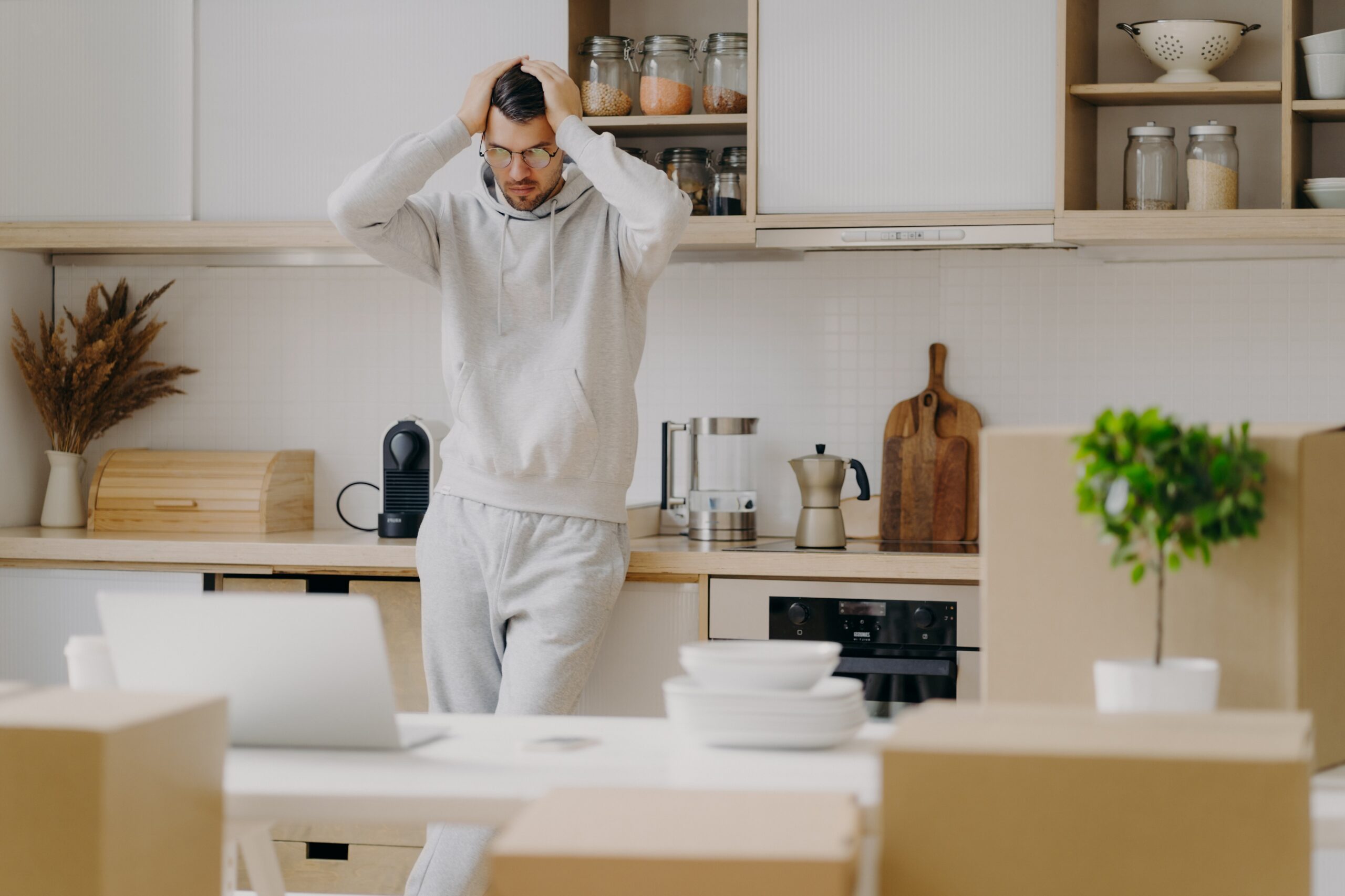 Frustrated Caucasian man faces financial problems, rents new apartment, looks with puzzlement at lap