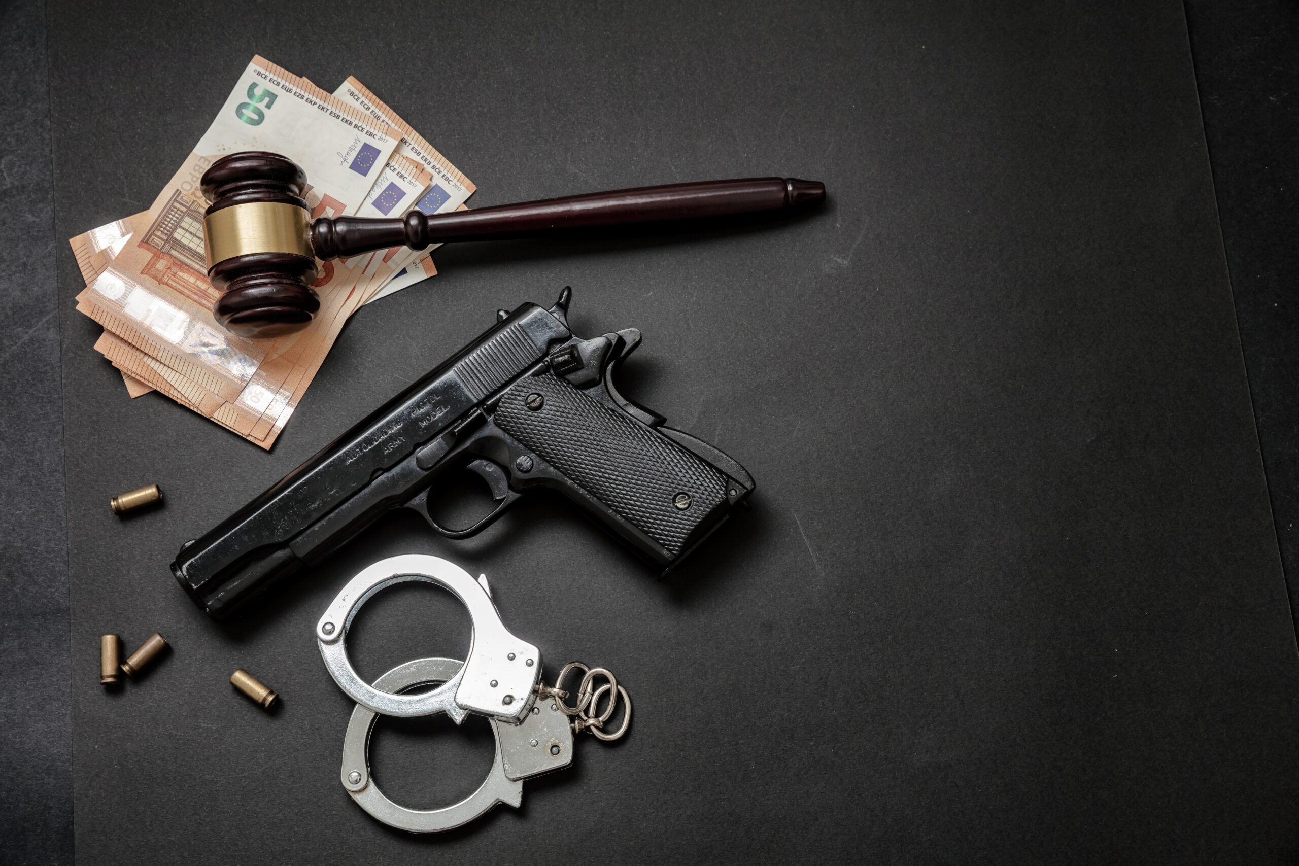 Judge gavel, handcuffs, banknotes and a 9mm pistol on black background,