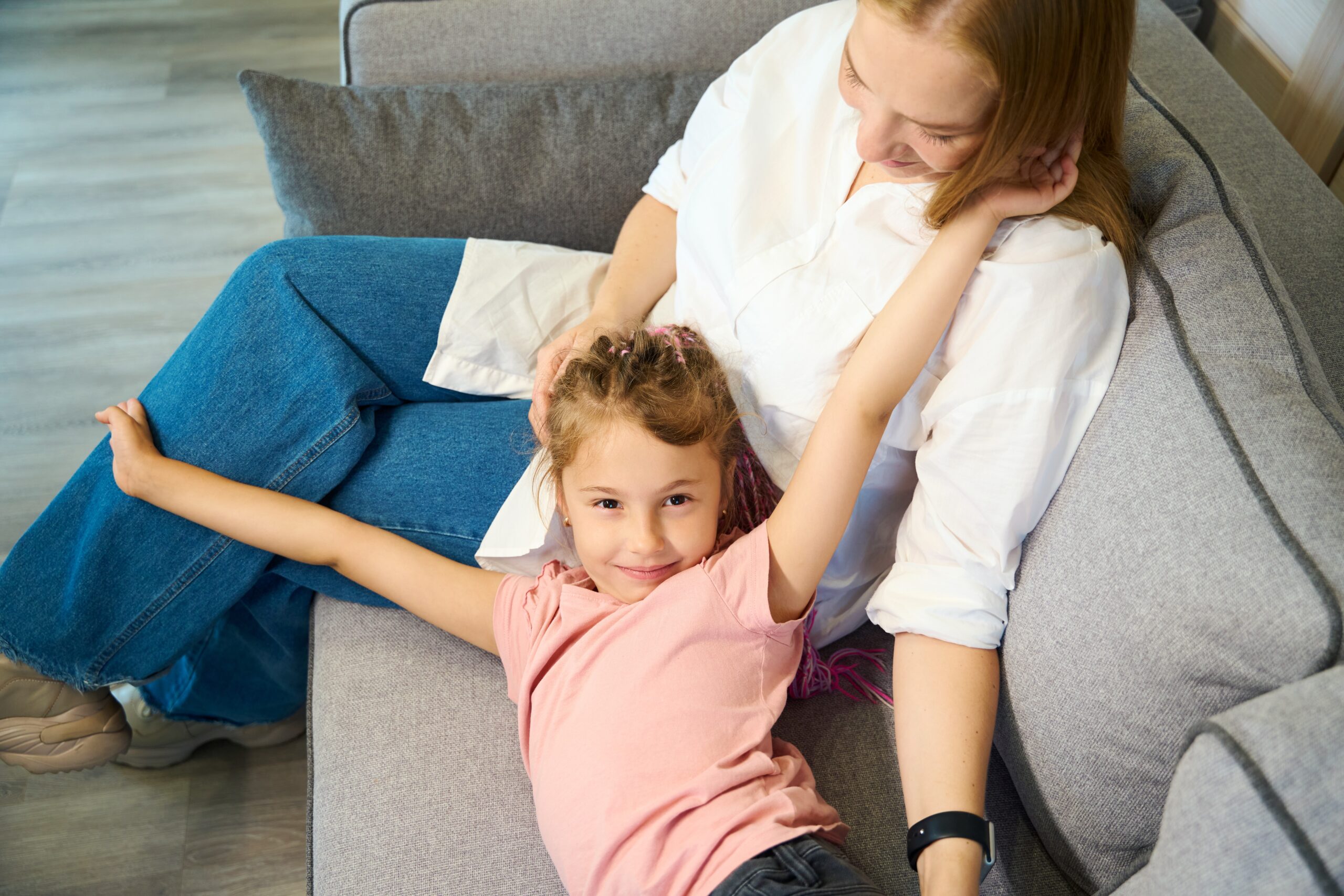 Little cute girl stretching her body lying on mothers knees on sofa