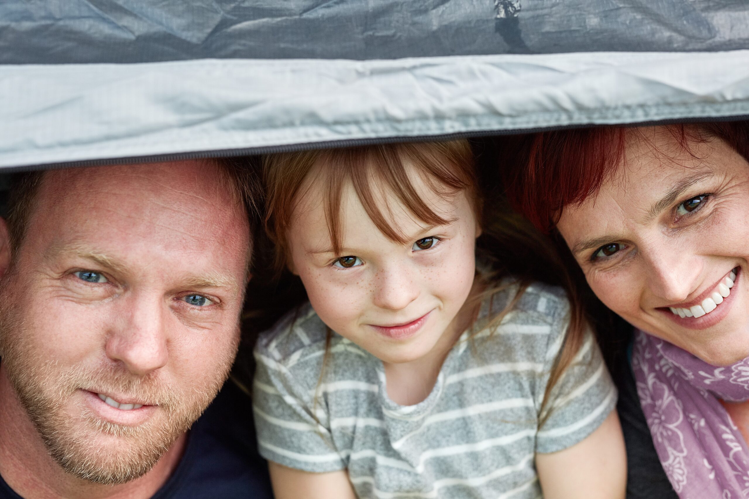 Portrait of a cute little girl and her parents sitting inside a tent together