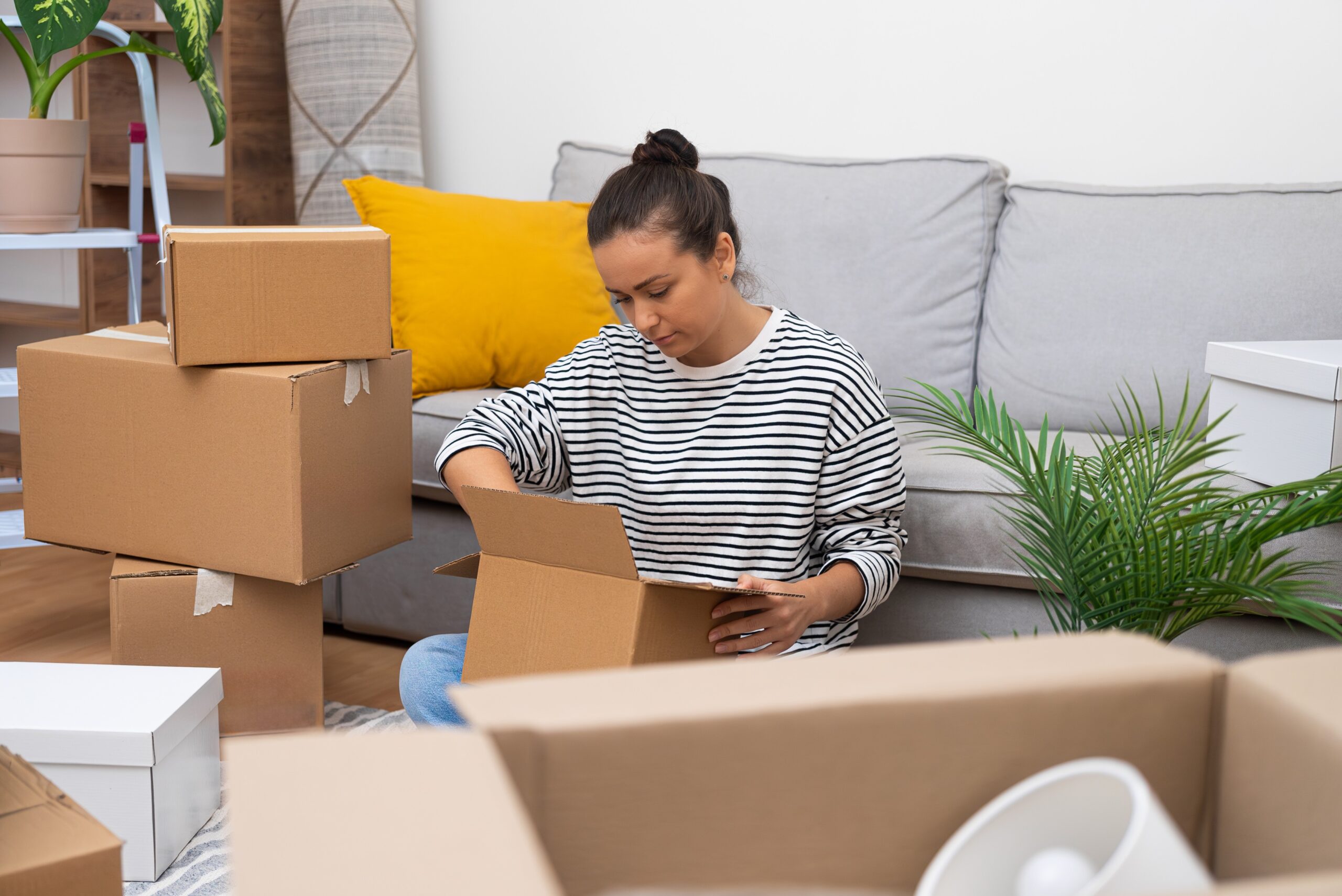 Woman takes out of box object for design near sofa in house