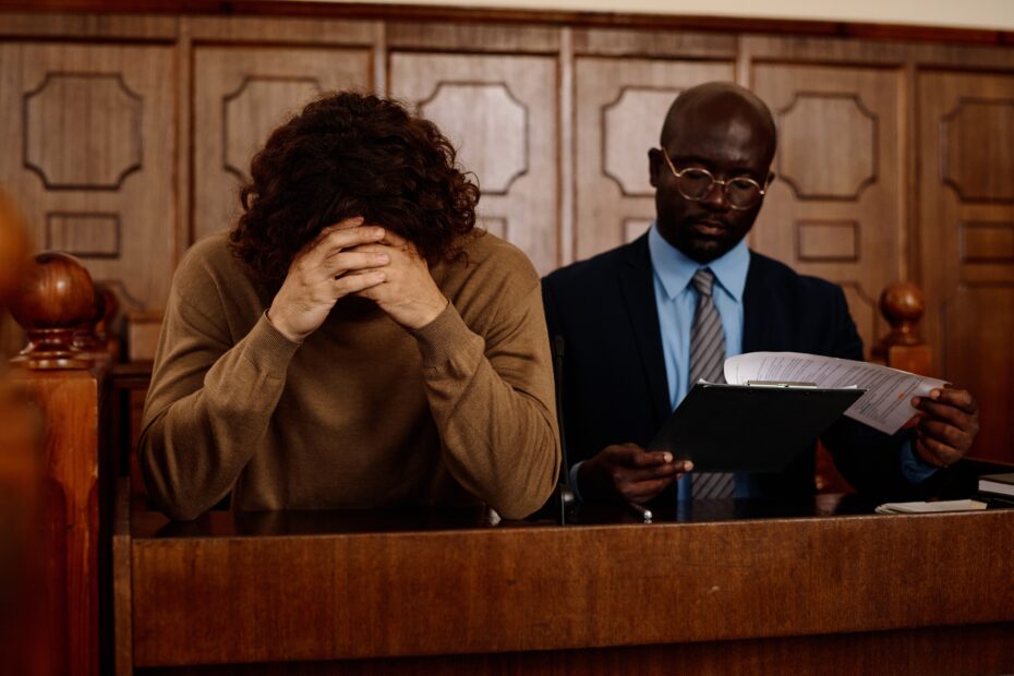 Young upset male suspect with clasped hands by his head sitting next to attorney